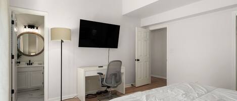 A bedroom with a bed, a desk with a chair, a TV, a lamp, and a mirror.