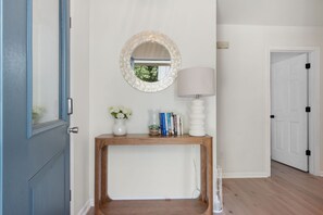 A hallway with a wooden console table, a round mirror, a white lamp, and a door with black handles. - Club Paradise: Pet Friendly, Soundside, Newly Updated! (Nags Head)