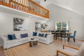 A spacious living room with a white sofa, a coffee table, and a dining area with a wooden table and chairs. - Club Paradise: Pet Friendly, Soundside, Newly Updated! (Nags Head)