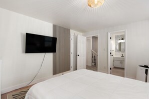 Une chambre dotée d’un grand lit, d’un téléviseur à écran plat fixé au mur, d’une armoire et d’une salle de bain visible à travers une porte ouverte.