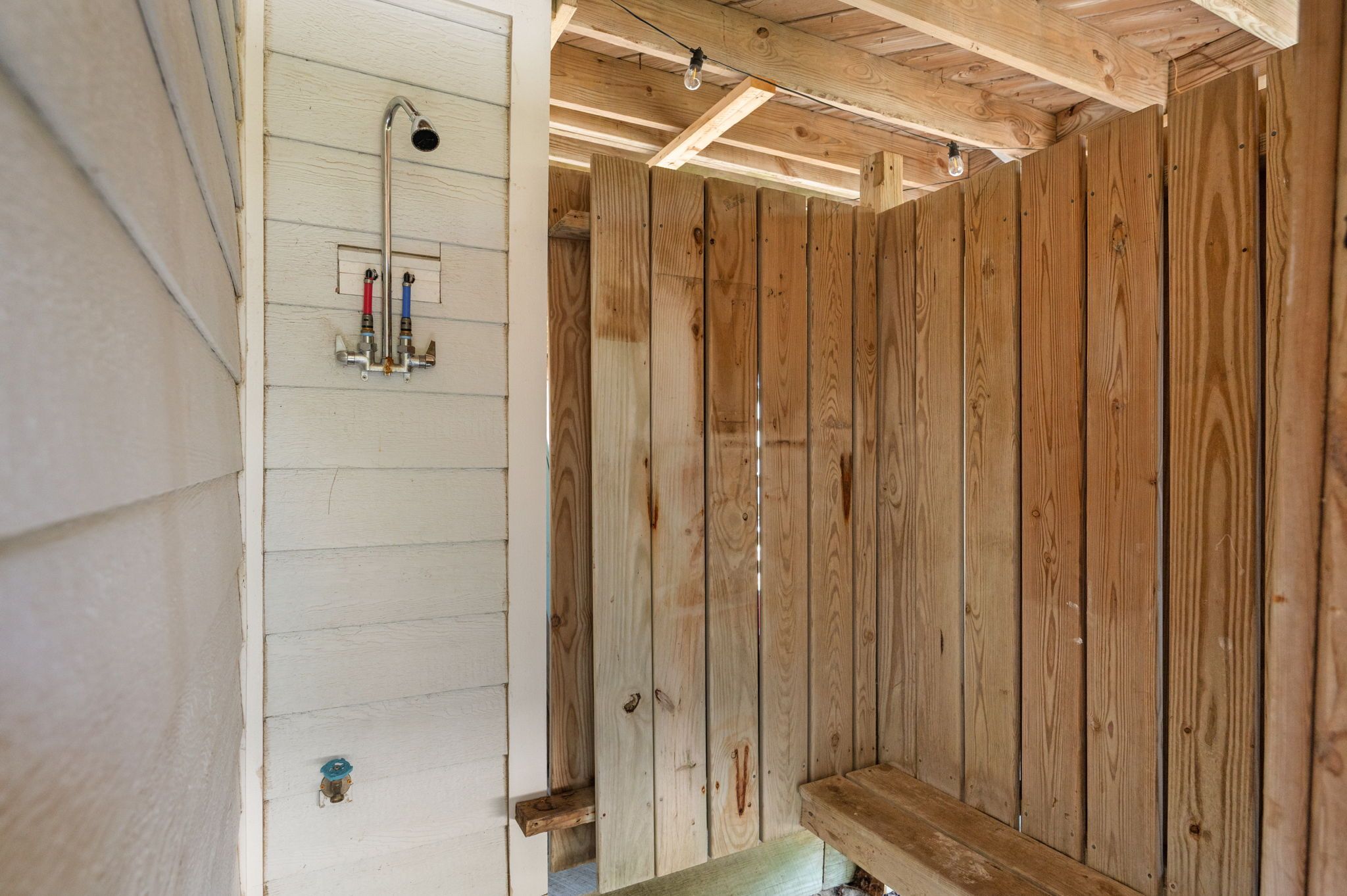 Interior de una cabaña de madera con zona de ducha, paredes de madera y un banco sencillo.