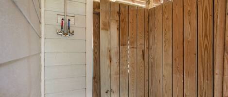 Interior de una cabaña de madera con zona de ducha, paredes de madera y un banco sencillo.