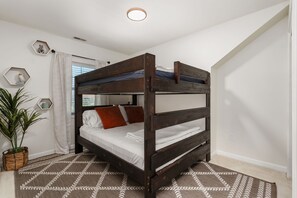 A bunk bed with a wooden frame, white bedding, and a geometric patterned rug.