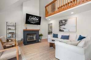 Un salon moderne avec une cheminée, des canapés blancs, un téléviseur fixé au mur et un escalier en bois.