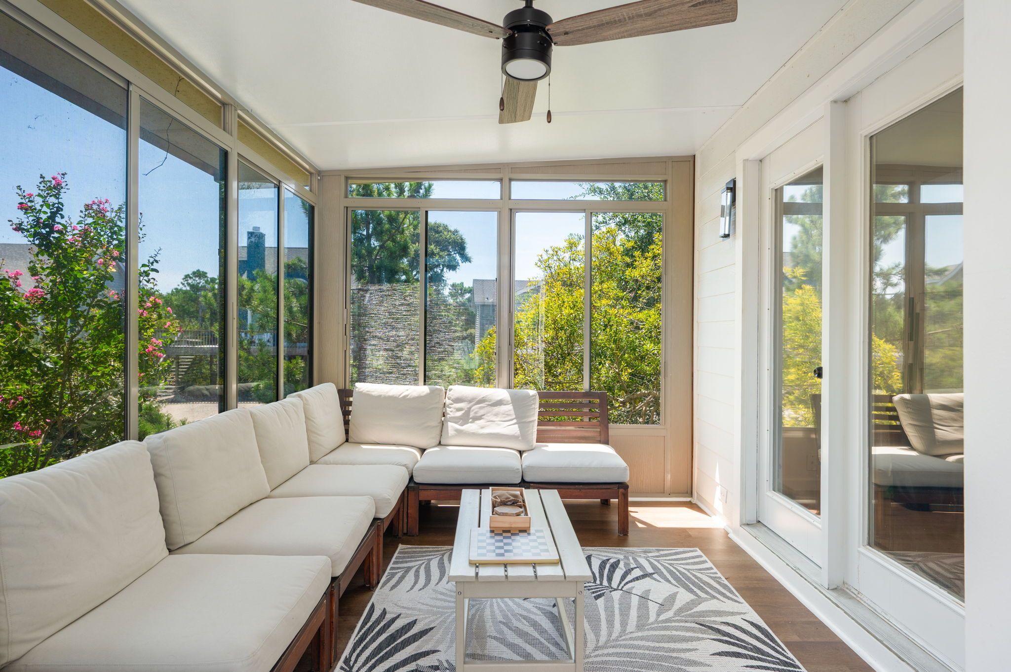 A sunlit room with a large sectional sofa, a wooden coffee table, and a ceiling fan.