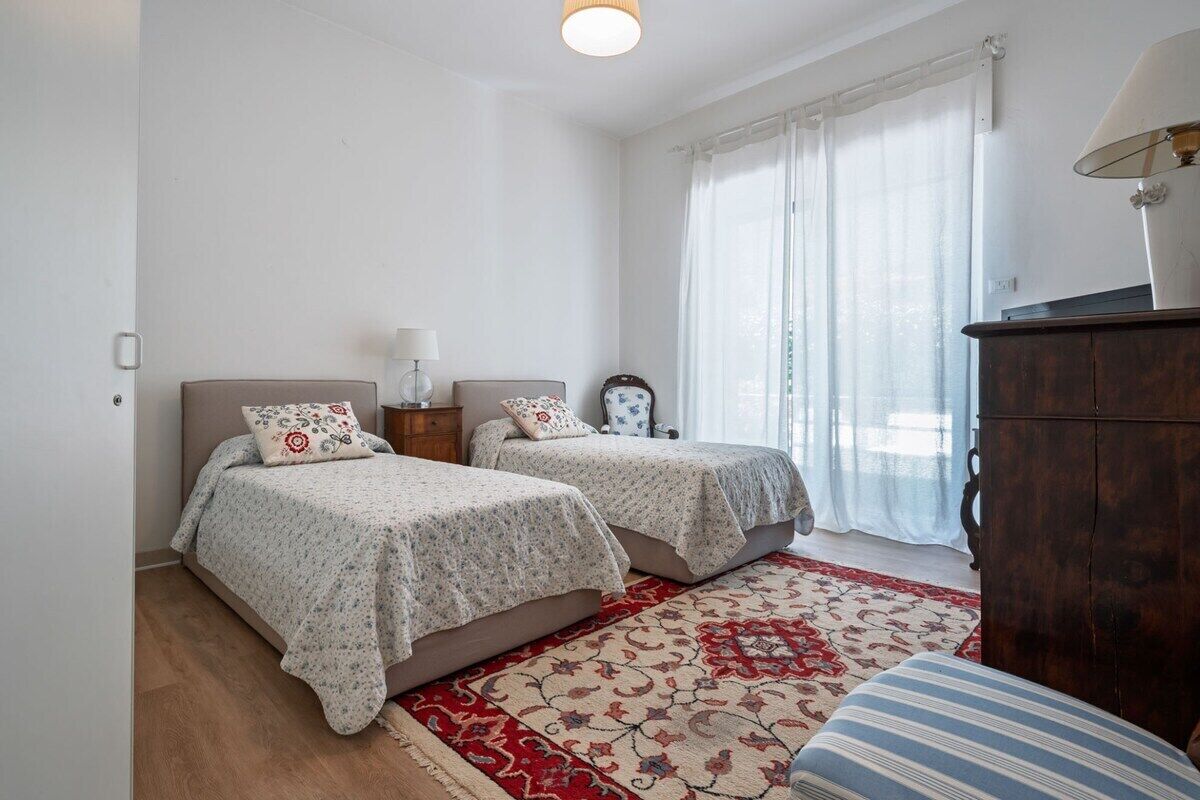Een slaapkamer met twee bedden, een houten dressoir en een rood tapijt met dessin.