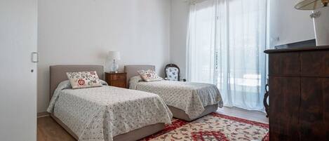 A bedroom with two beds, a wooden dresser, and a red patterned rug.