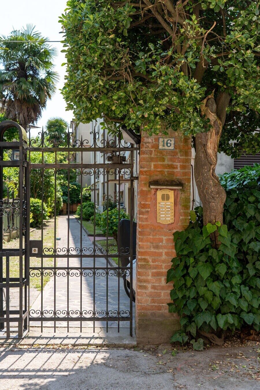 A gated entrance with a brick wall and a number plaque, surrounded by lush greenery.