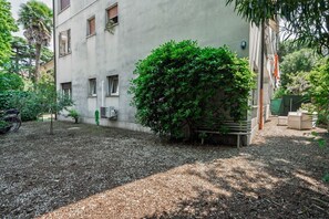 Ein Innenhof mit einem Gebäude, Kiesgrund und einem großen Busch.