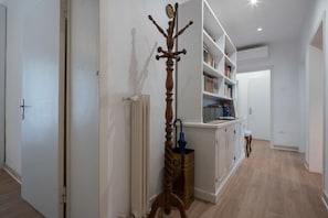 A hallway with a coat rack, a radiator, a bookshelf, and a door.