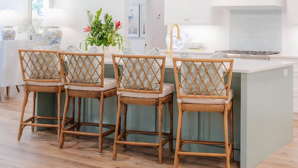 Una cocina moderna con una isla central, cuatro sillas de mimbre e iluminación colgante.