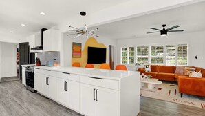 Una cucina moderna con mobili bianchi, un'isola centrale e un'area pranzo con sedie arancioni.