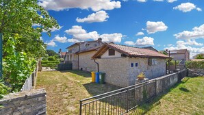 Une maison en pierre avec un toit de tuiles, une cour clôturée et un ciel bleu dégagé.