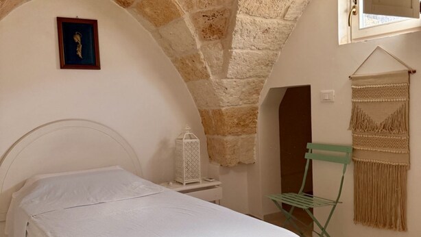 Une chambre avec un lit, une table de chevet, une décoration murale en macramé suspendue et un plafond en forme d’arc en pierre.