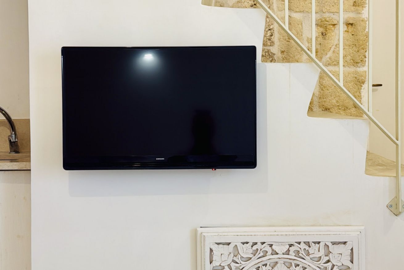 Een flatscreen televisie bevestigd aan een witte muur, met een wit decoratief paneel eronder, en een stenen trap aan de rechterkant.