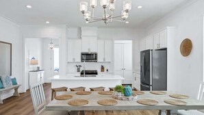 A modern kitchen with white cabinetry, a central island, and a stainless steel refrigerator. - Tranquil Tides Orange Beach Getaway (Orange Beach)