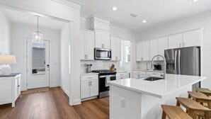 A modern kitchen with white cabinetry, stainless steel appliances, and a central island with stools. - Tranquil Tides Orange Beach Getaway (Orange Beach)