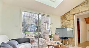 A living room with a sofa, a coffee table, a TV, and a stone wall. - ClémentIne - ELVEN - Gîte (ELVEN)