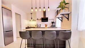 Une cuisine moderne dotée d’un îlot central, de tabourets de bar, d’un réfrigérateur en acier inoxydable et de luminaires suspendus.