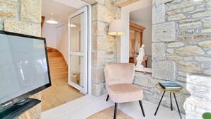 Un salon moderne avec un mur en pierre, un téléviseur, un fauteuil rose et une petite table sur laquelle se trouve un livre.