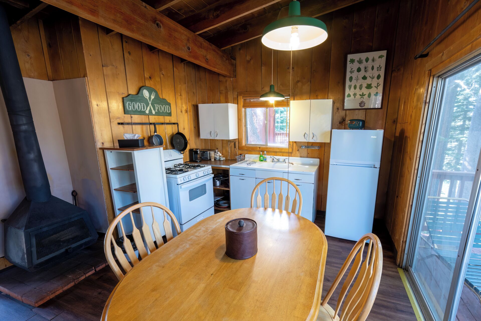 A cozy wooden cabin kitchen with a stove, sink, refrigerator, and a dining table with chairs.