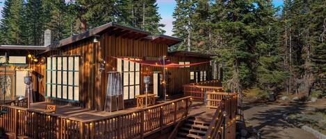 A wooden cabin with a deck, surrounded by tall trees.