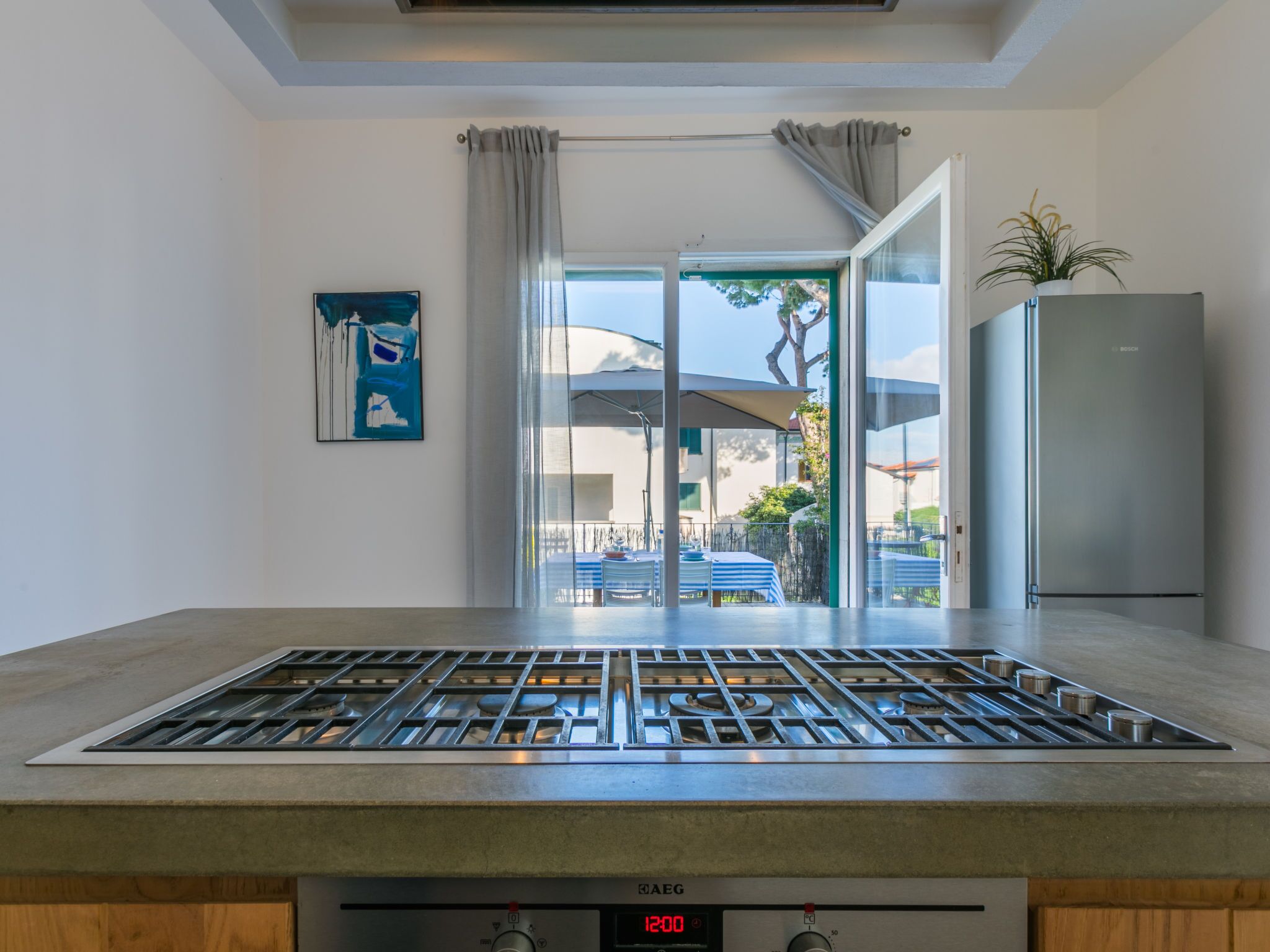 Una cocina moderna con estufa a gas, un refrigerador Bosch y vistas al patio exterior.