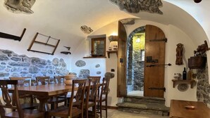 Un coin repas rustique avec un mur en pierre, des meubles en bois et une arche en pierre menant à une porte.