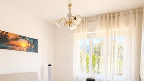 Une chambre à coucher avec un lit, un tableau, un luminaire au plafond, une fenêtre avec des rideaux et un revêtement de sol à motifs.