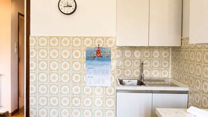 Une petite cuisine équipée d’un évier, de placards et d’une horloge murale.