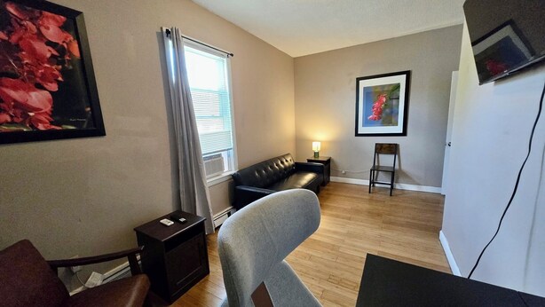 Un salon comprenant un canapé, un fauteuil, une petite table, une lampe et un téléviseur fixé au mur.