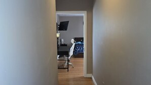 Un couloir étroit, doté d’un plancher en bois, mène à une chambre à coucher qui contient un lit et un bureau.