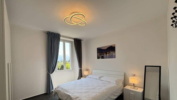 Een moderne hotelkamer met een groot bed, nachtkastjes, een spiegel en uitzicht op een stadsgezicht.