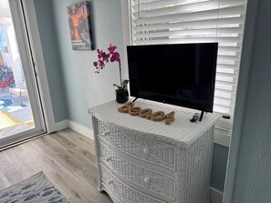 A room with a white wicker TV stand, a flat-screen TV, a potted orchid, and a framed picture on the wall.