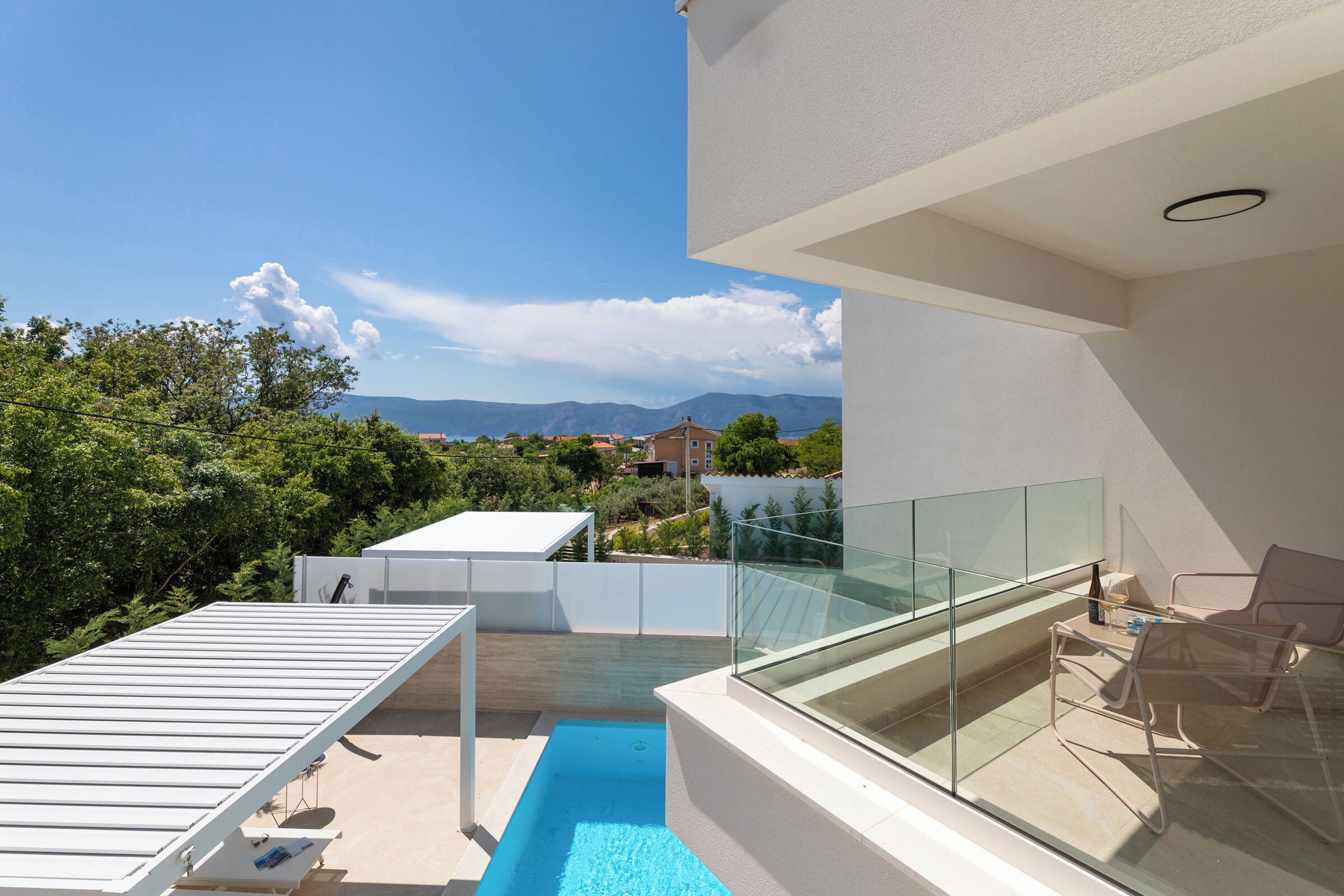Un balcon moderne avec une balustrade en verre, une piscine et du mobilier d’extérieur.