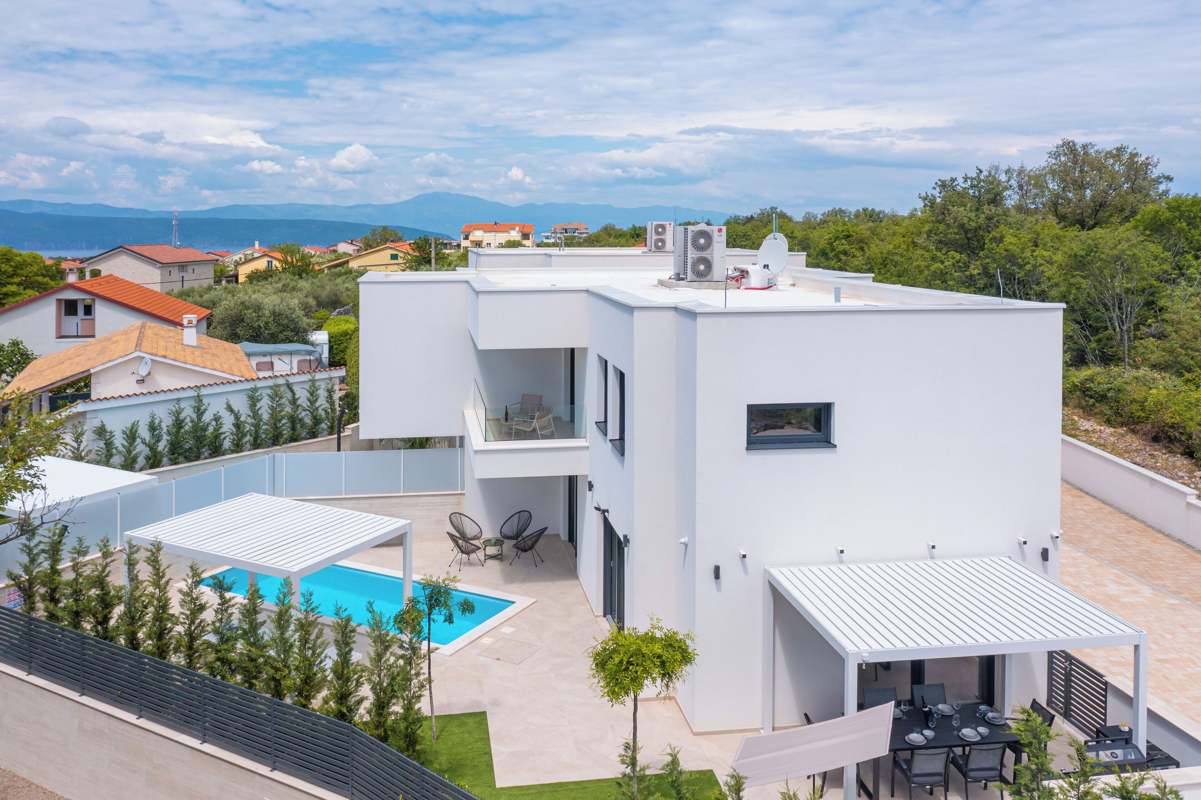 A modern two-story house with a swimming pool, outdoor seating, and a view of the surrounding landscape.
