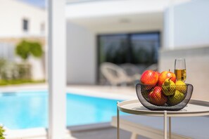 Une table ronde avec un panier de fruits et un verre de vin, près d’une piscine.