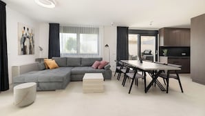 En moderne stue med en grå hjørnesofa, et sofabord og et spiseområde med et bord og stole.