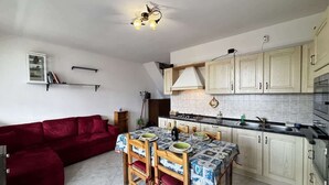 A compact kitchen with a dining table, chairs, and a red sofa. - Alloggio Pradella - Larihome A97 (Gravedona ed Uniti)