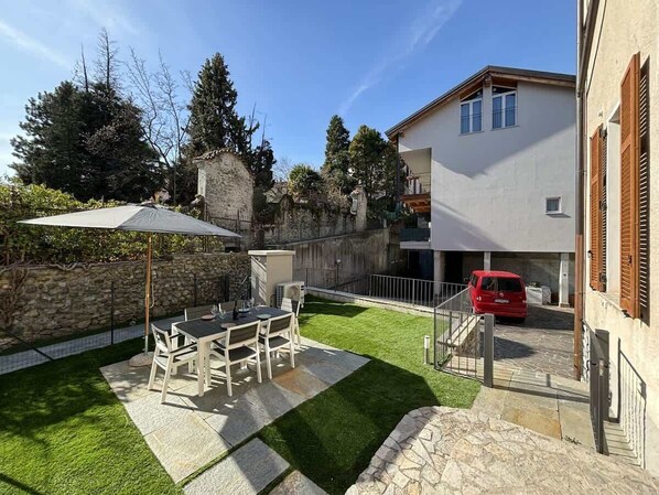 A residential property with a patio, outdoor seating, a stone wall, and a red car parked in the driveway. - Ancient Gravedona - Apt Maria - Larihome A41 (Gravedona)