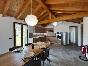 Uma cozinha moderna com vigas de madeira, uma área de jantar com mesa de madeira e vista para o exterior.