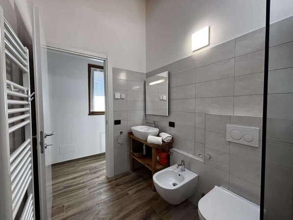 Uma casa de banho moderna com chão de madeira, um lavatório branco, um bidé e um espelho.