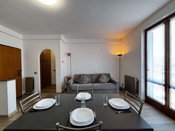 Un comedor con una mesa dispuesta para cuatro personas, un sofá, un radiador y una ventana con vistas.