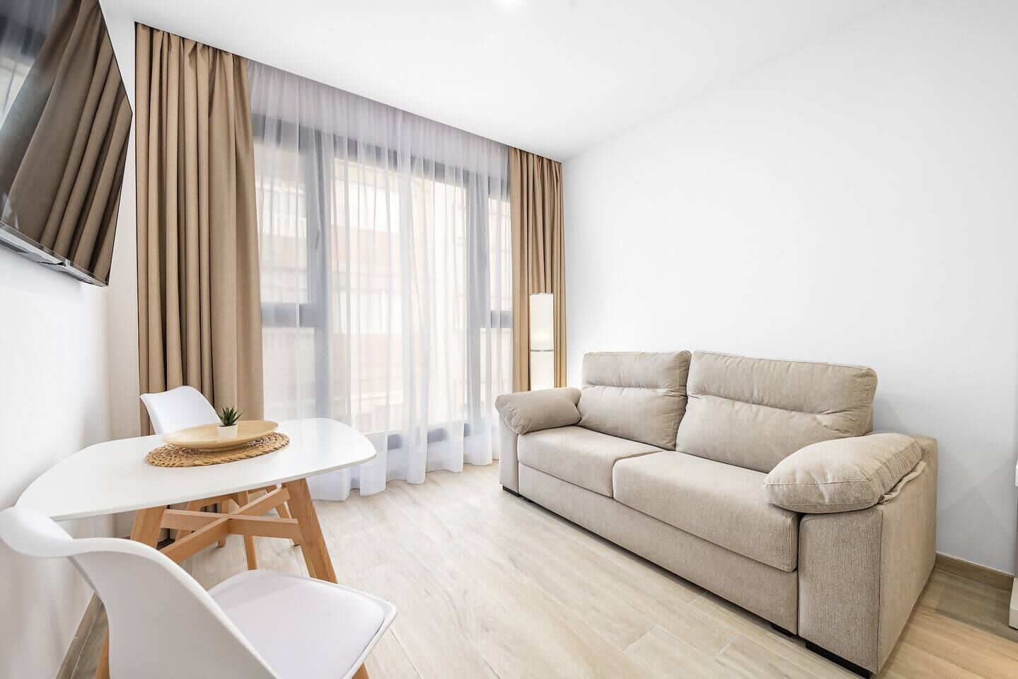 Un salon moderne avec un canapé beige, une table blanche avec des chaises et des rideaux légers.