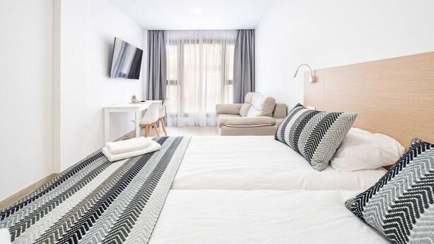 Habitación de hotel con cama, escritorio, silla, sofá y televisor montado en la pared.