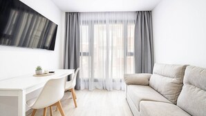 Una sala de estar moderna con un sofá blanco, un escritorio con una silla y un televisor montado en la pared.