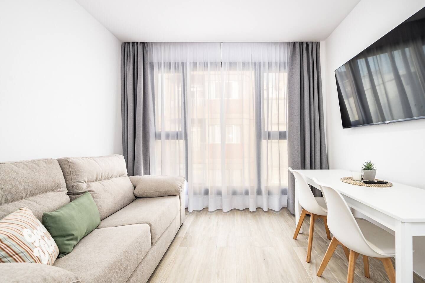 Een moderne woonkamer met een bank, een eettafel met stoelen en een aan de muur bevestigde televisie.