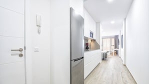 Ein schmaler Flur mit einem Edelstahlkühlschrank, einem weißen Telefon und einer kleinen Küchenzeile mit Mikrowelle und Spüle.