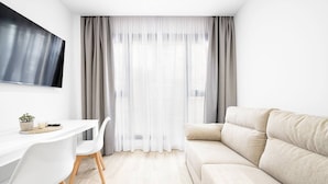 Ein modernes Wohnzimmer mit einem weißen Sofa, einem Esstisch mit Stühlen und einem an der Wand befestigten Fernseher.
