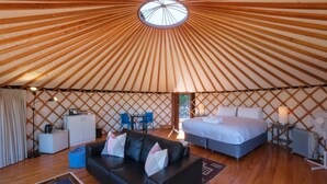 Interieur van een joert met een bed, bank en zithoek, met een houten spijlenwand en een rond dakraam.